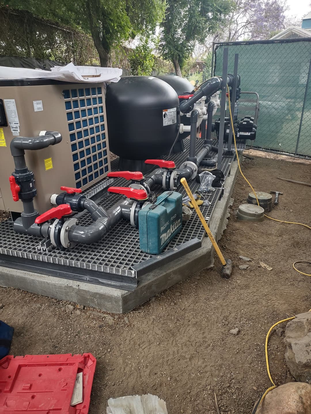 Pump and filtration system with pipes and tools on a gravel base outdoors.