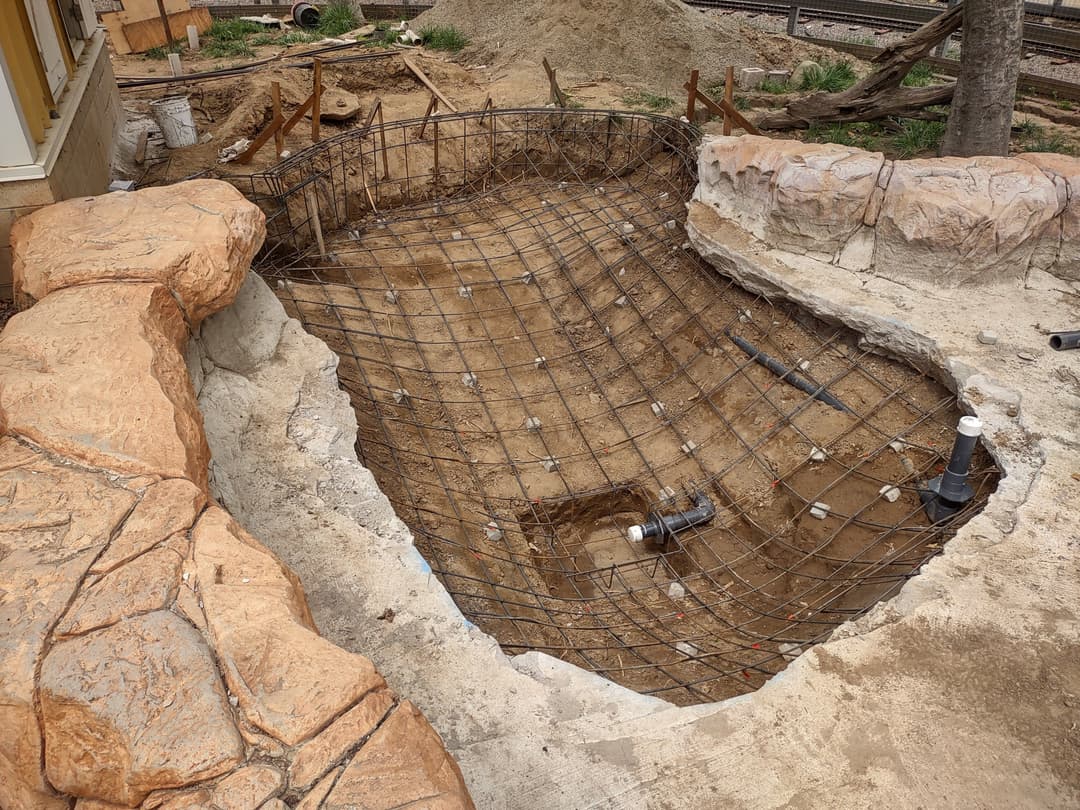 Wire-frame structure for a pond under construction, featuring rocky edges and plumbing components.