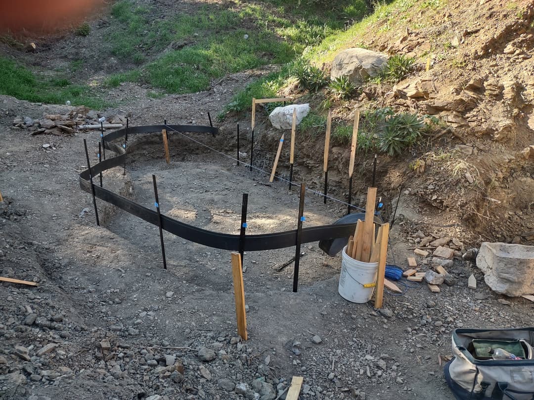 Foundation formwork in a gravel area, surrounded by tools and wooden stakes for construction.
