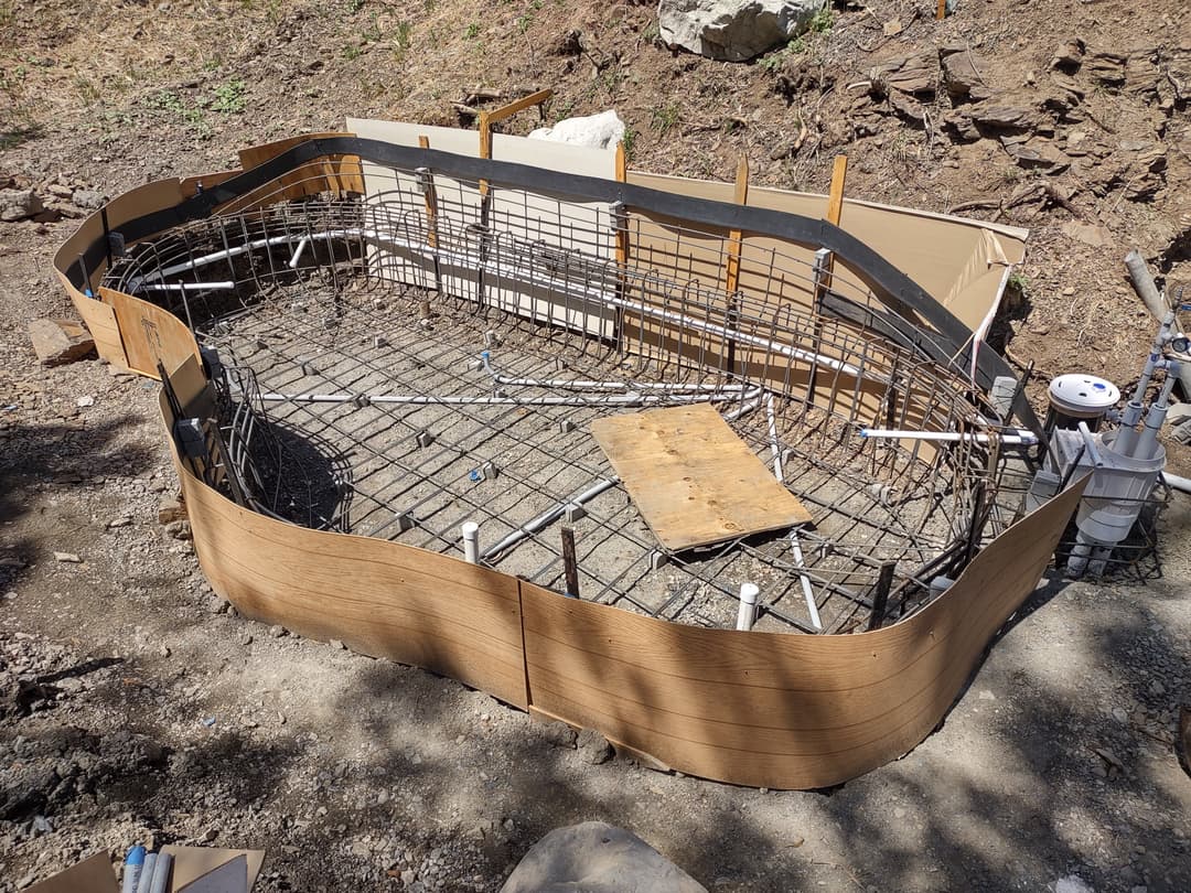 Construction of a curved swimming pool frame with metal rebar and plumbing installed.