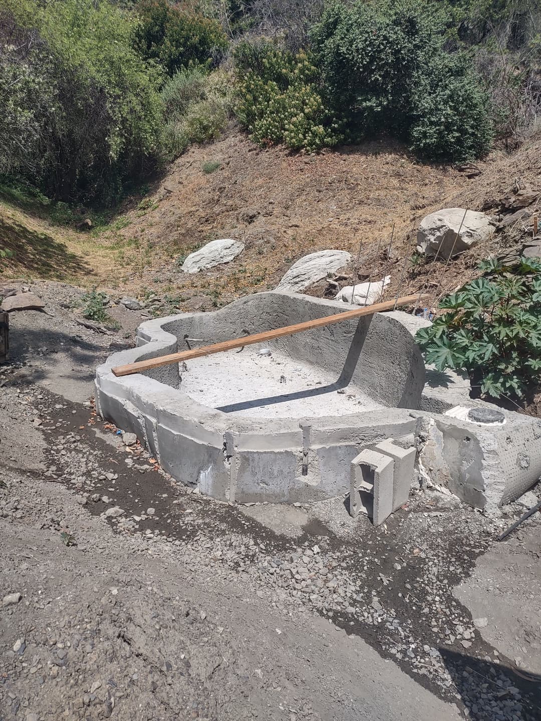 Concrete foundation partially completed in a hilly outdoor area with vegetation.