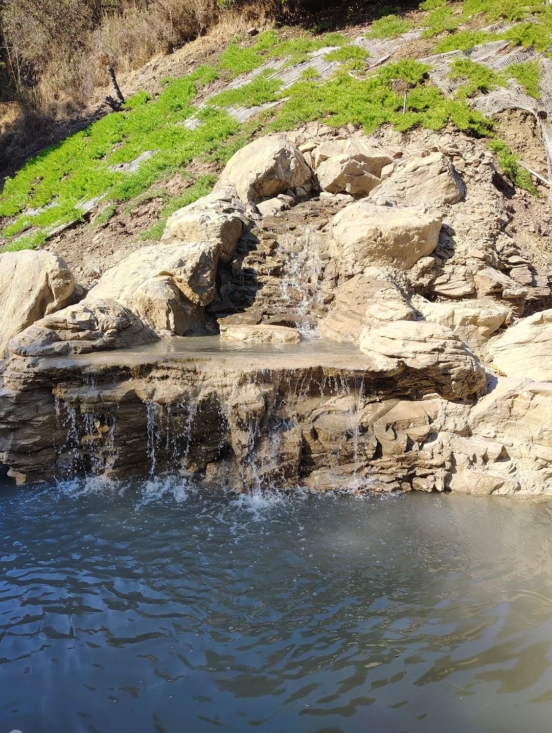 Waterfall cascading over rocks into a serene pond surrounded by greenery.