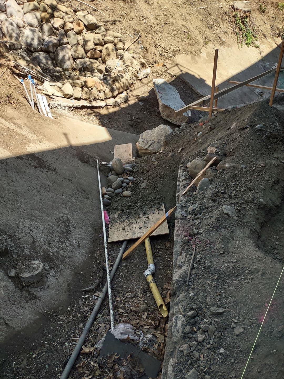 Construction site with excavated earth, gravel, and wooden planks in a rocky area.