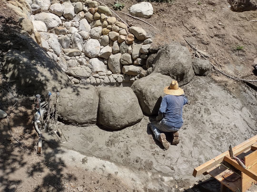 Person applying concrete to create a stone landscape feature in a garden.