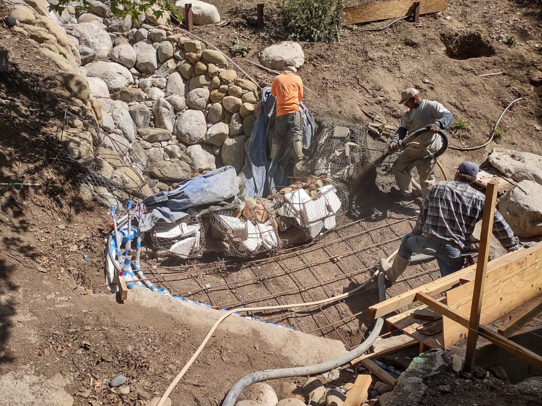 Workers installing rebar and rocks for a landscape structure in a construction site.