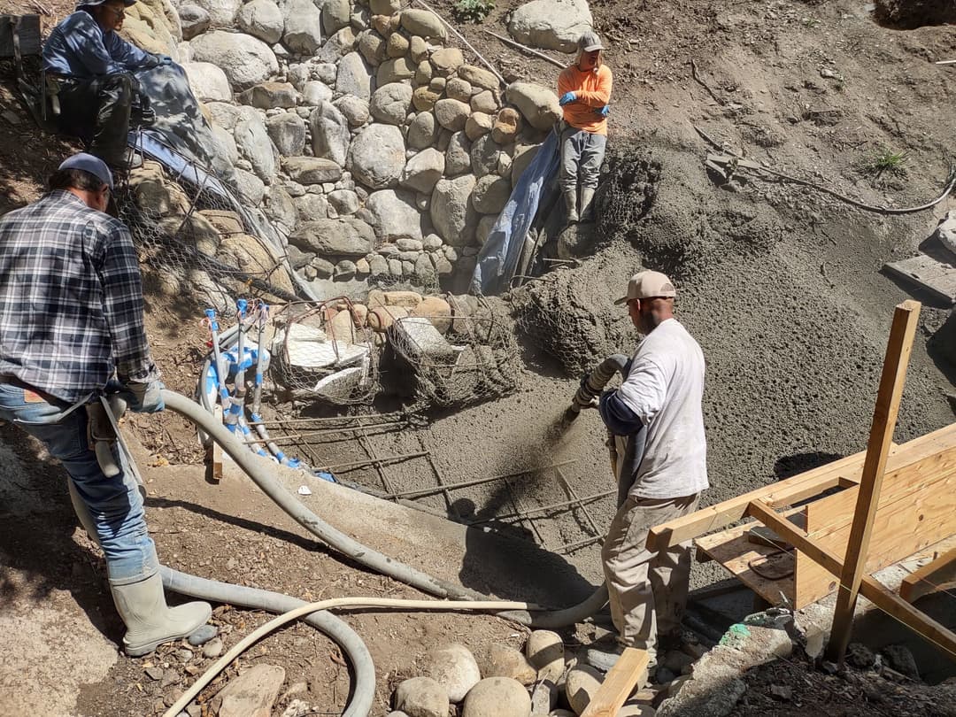 Workers pouring concrete for a stone wall foundation in a construction site.