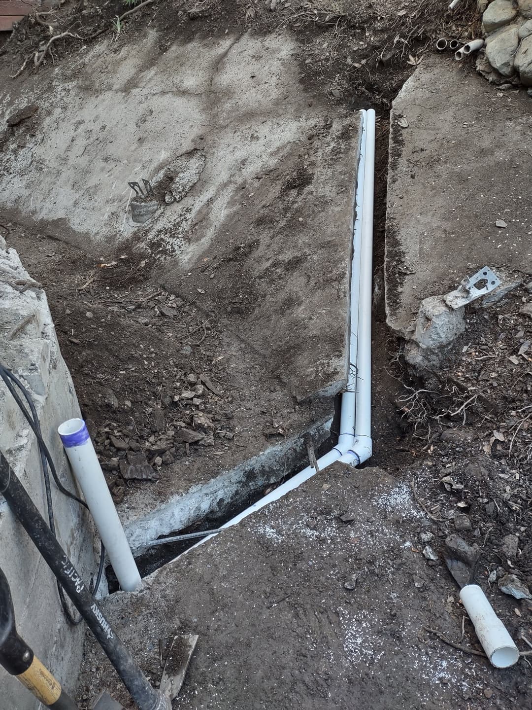 Excavated area with new white PVC pipes installed for drainage or plumbing system.