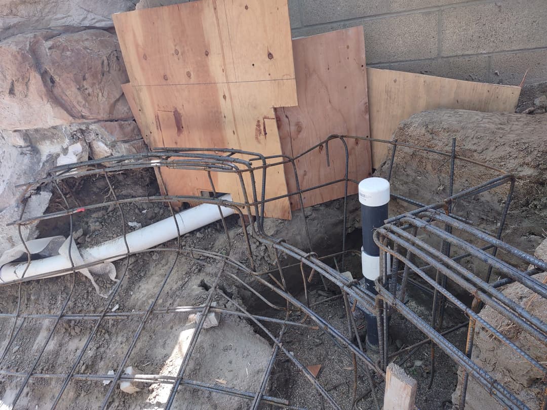 Construction site with rebar framework, drainage pipe, and wooden boards for support.