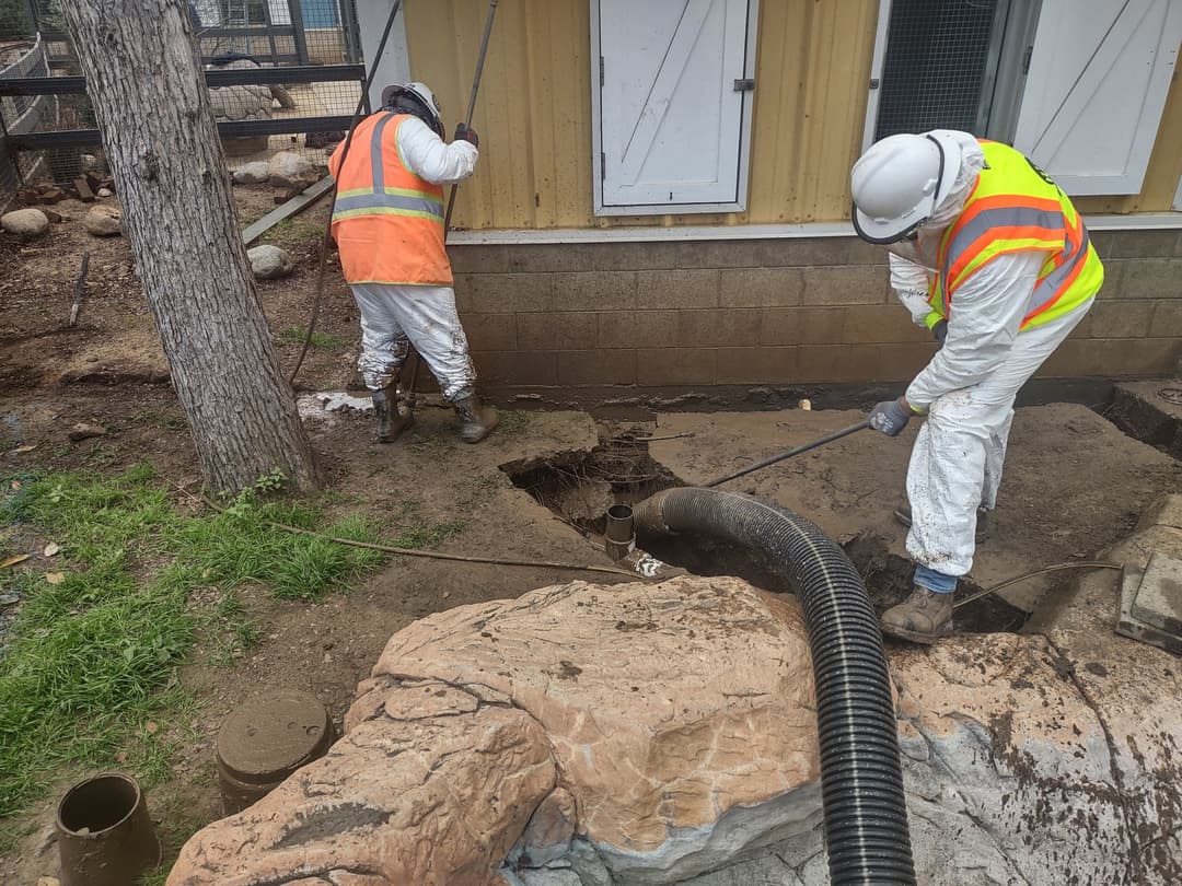 Workers in safety gear repairing a drainage system at a construction site.