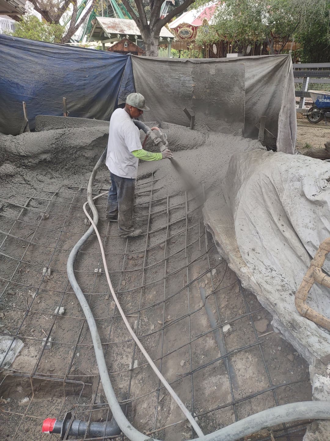 Construction worker spraying concrete over rebar framework at a building site.