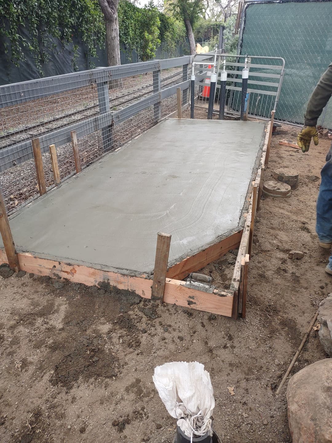 Concrete slab being poured on a wooden frame, outdoors with construction tools nearby.