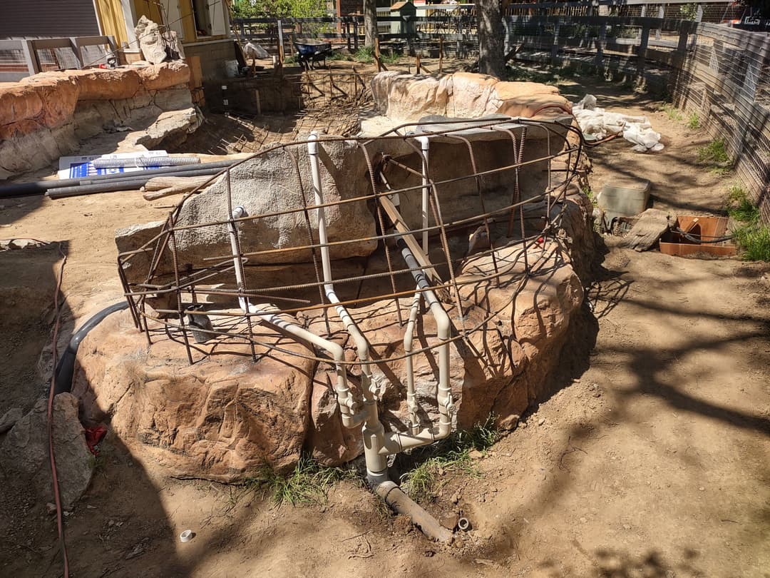 Construction site showcasing a rock formation with reinforcing metal framework and plumbing pipes.