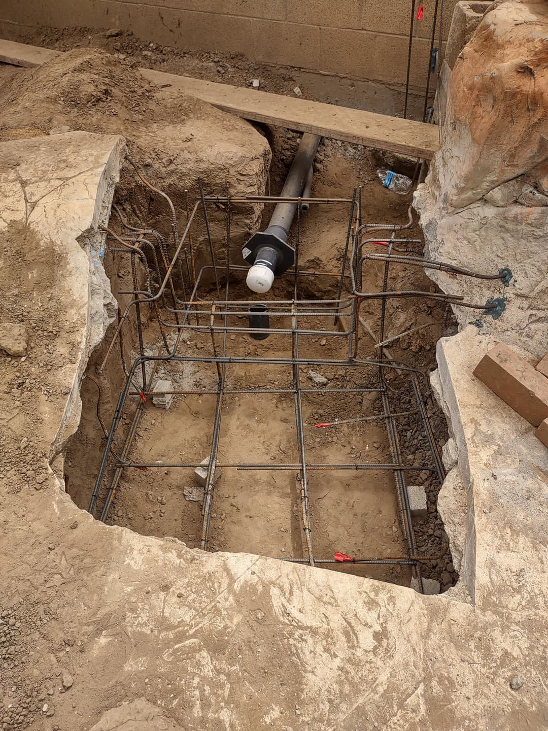 Excavated site with rebar framework and plumbing pipe ready for concrete foundation installation.