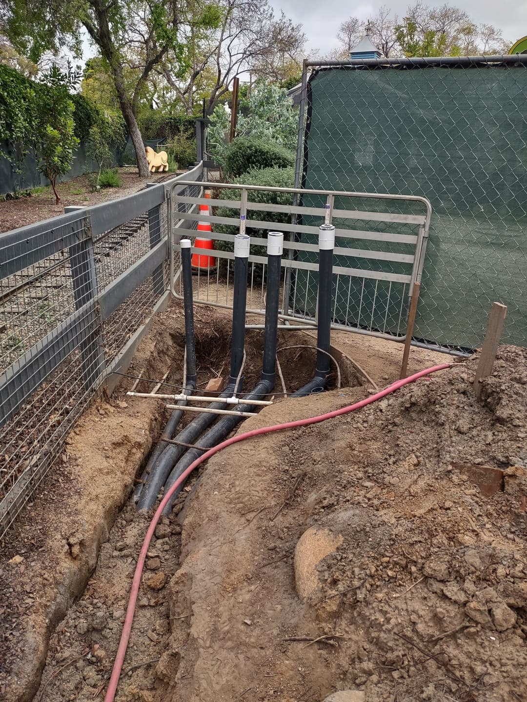 Installation of drainage pipes in a trench surrounded by fencing and landscaping.