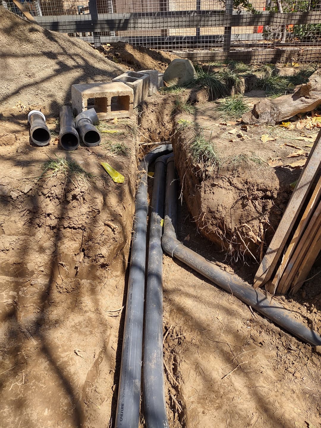 Trenched area with installed black pipes and cinder blocks among dirt and grass.