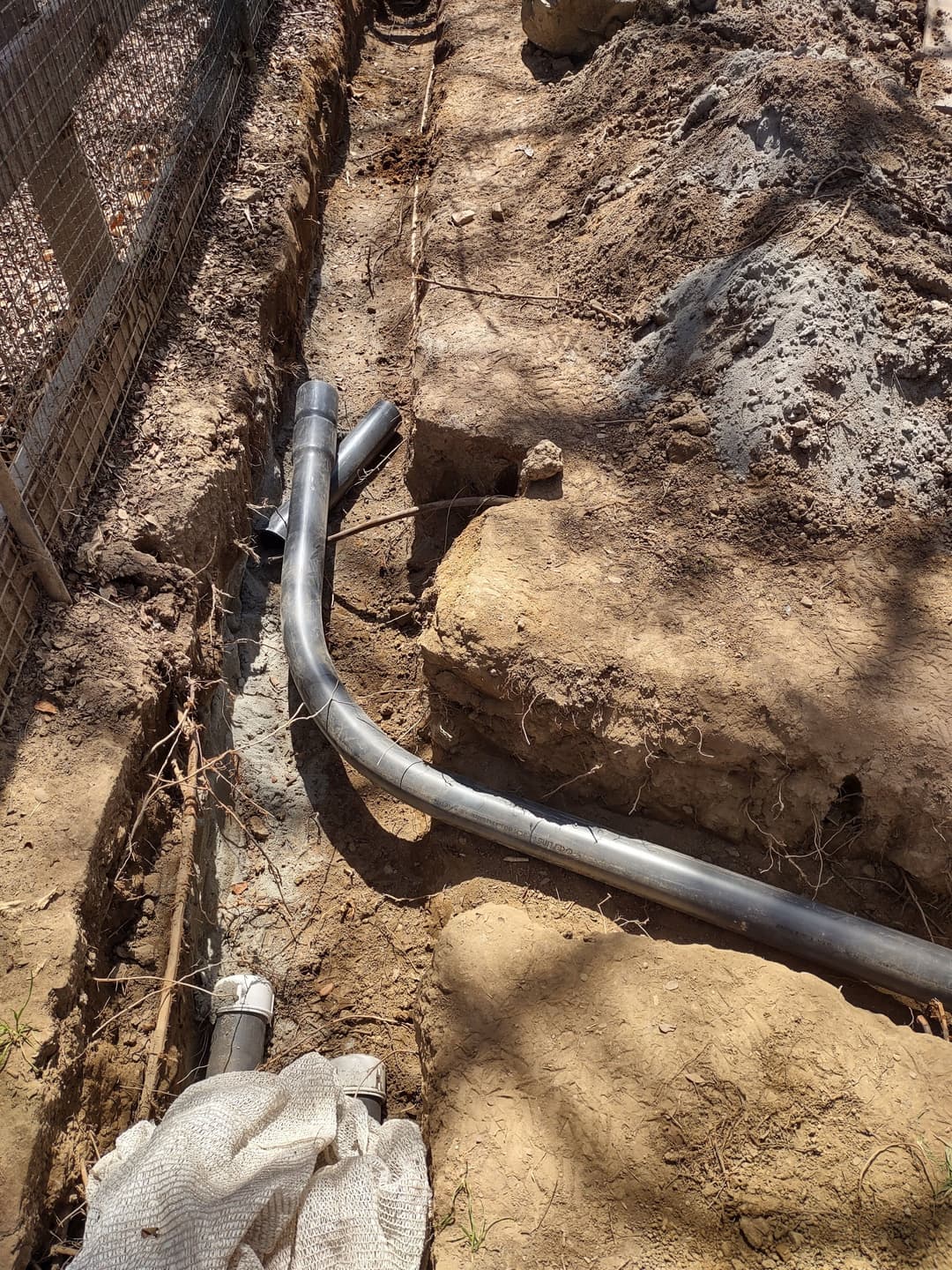 Installation of underground drainage pipes in a trench surrounded by soil and gravel.