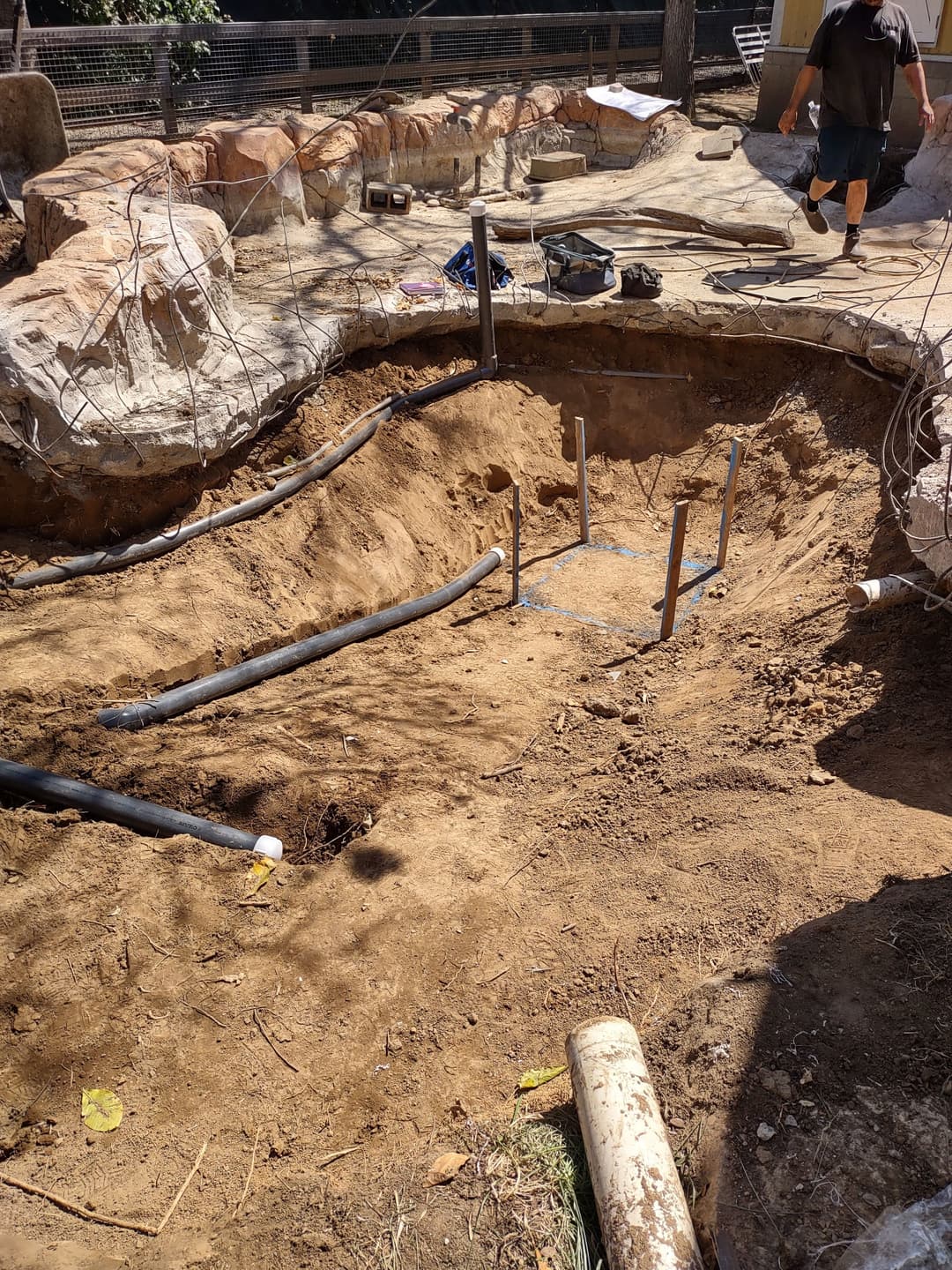 Excavated area with pipes for landscaping project, tools, and rocky surroundings.