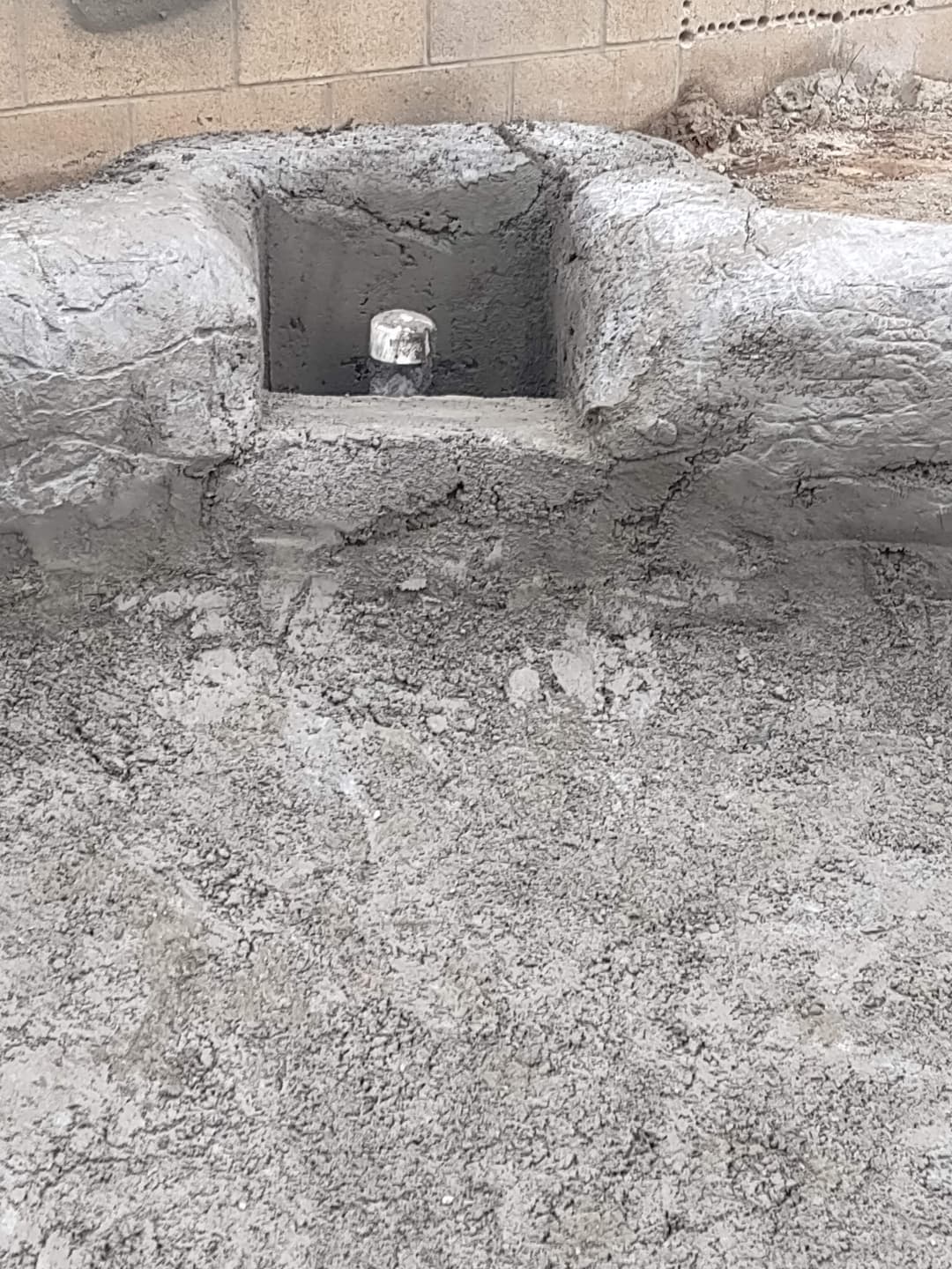 Freshly poured concrete with a concrete block and drainage pipe in construction area.