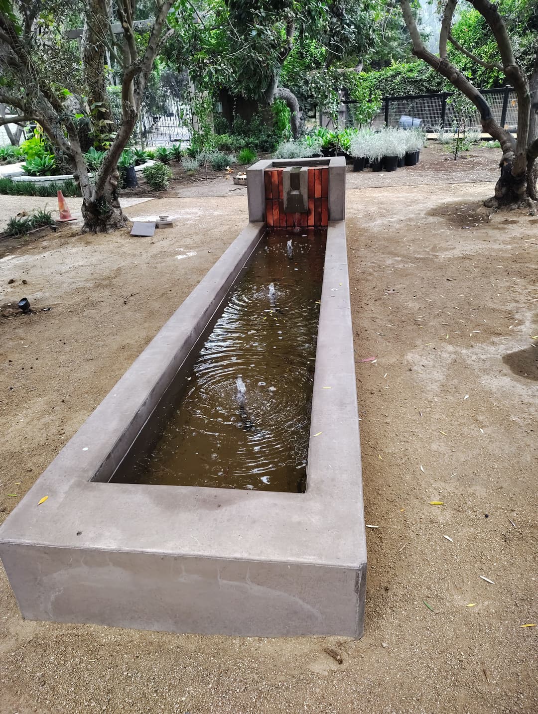 Modern rectangular water feature in a landscaped garden surrounded by trees.