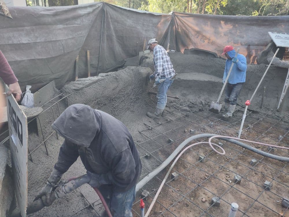 Construction workers pouring concrete at a building site with rebar framework visible.