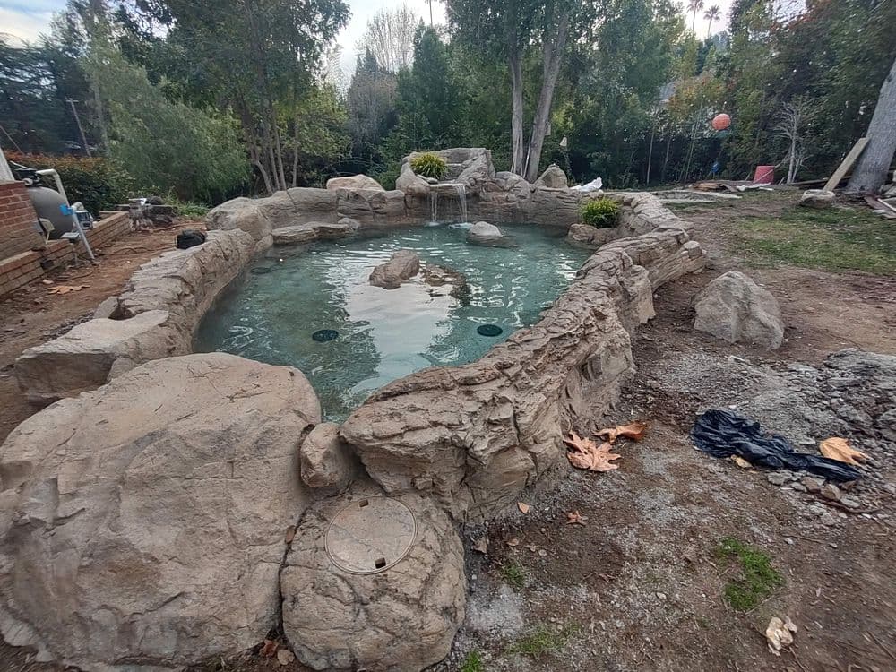Natural stone pond surrounded by landscaping and trees, featuring clear water and boulders.