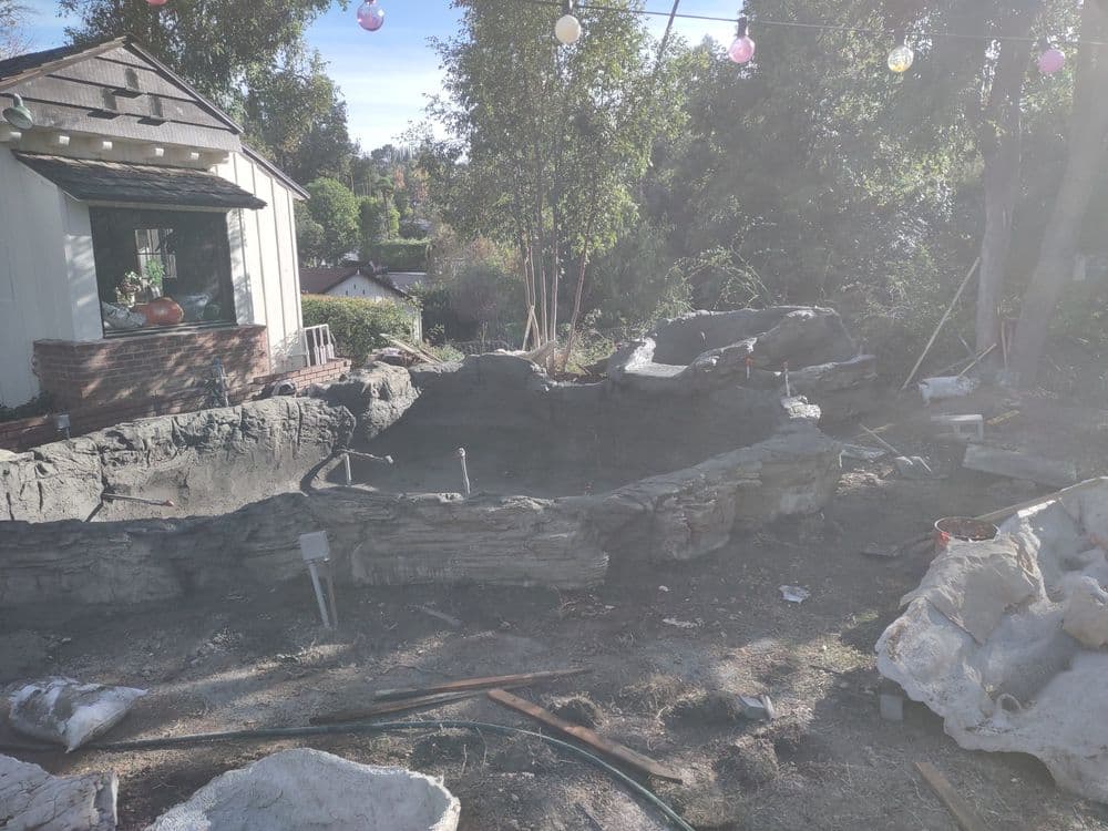 Backyard under renovation with stone landscape, unfinished pool, and construction tools.