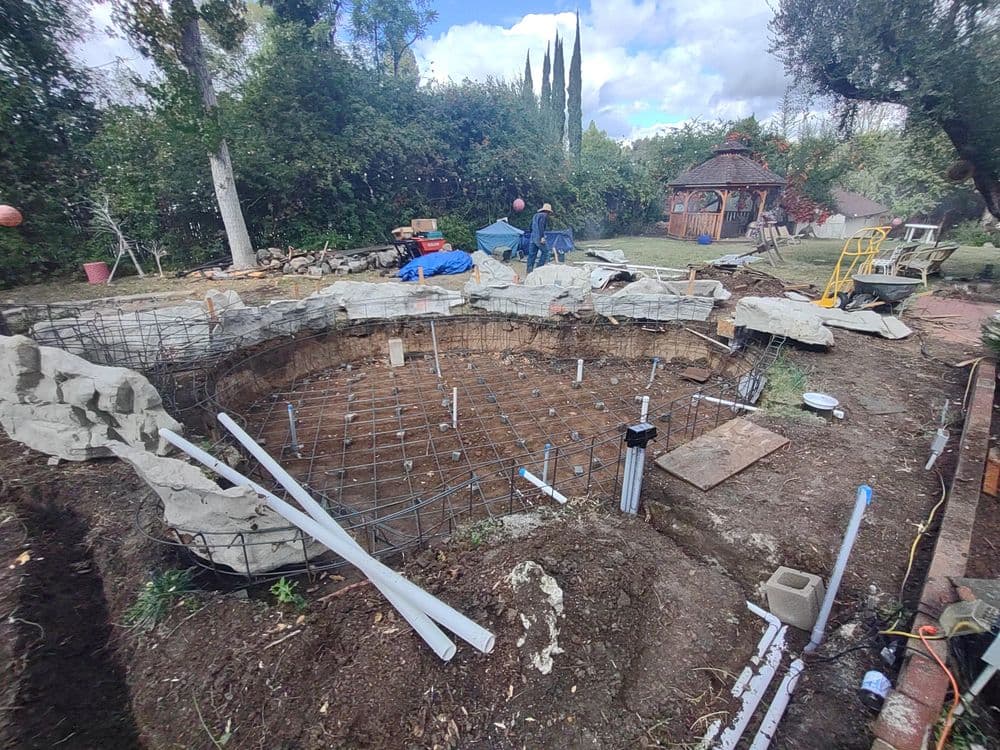 Construction site for a pond featuring rebar, rock formations, and landscaping in progress.
