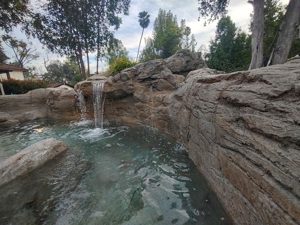 Relaxing rock waterfall feature in a tranquil pool surrounded by lush greenery.